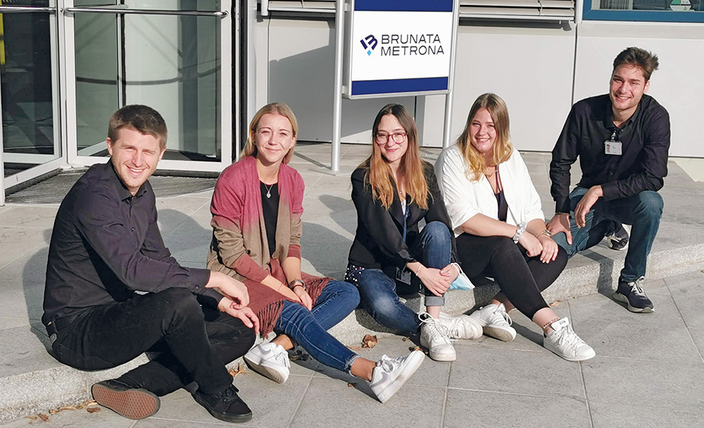 5 junge MEnschen sitzen auf einem Borstein vor dem Firmengebäude Eingang 5 junge MEnschen sitzen auf einem Borstein vor dem Firmengebäude Eingang