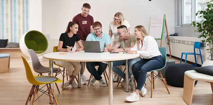 Mehrere Personen sitzen um einen Tisch herum und sehen auf einen Laptop. Mehrere Personen sitzen um einen Tisch herum und sehen auf einen Laptop.