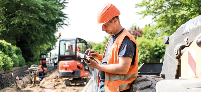Person in Warnweste mit Helm tippt etwas ins Tablet auf der Baustelle