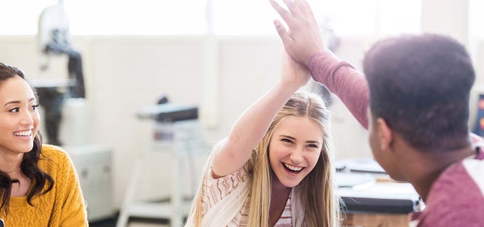 Drei Personen, zwei davon geben sich ein High-Five. Drei Personen, zwei davon geben sich ein High-Five.