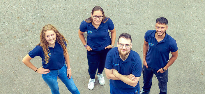 Vier Auszubildende in blauen Poloshirts schauen nach oben in die Kamera Vier Auszubildende in blauen Poloshirts schauen nach oben in die Kamera