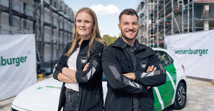Zwei Personen lächeln in die Kamera und stehen Rücken an Rücken. Zwei Personen lächeln in die Kamera und stehen Rücken an Rücken.