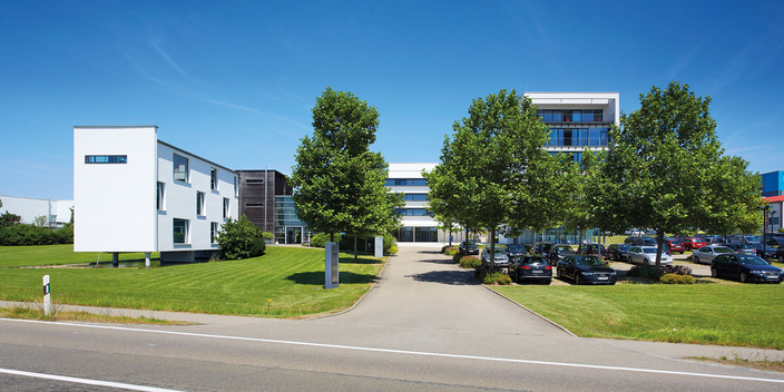 Firmengebäude der FNT GmbH mit Parkplatz unter Bäumen Firmengebäude der FNT GmbH mit Parkplatz unter Bäumen