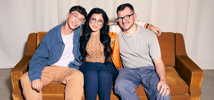 Gruppenbild mit drei jungen Menschen, die auf einem Sofa zusammensitzen
