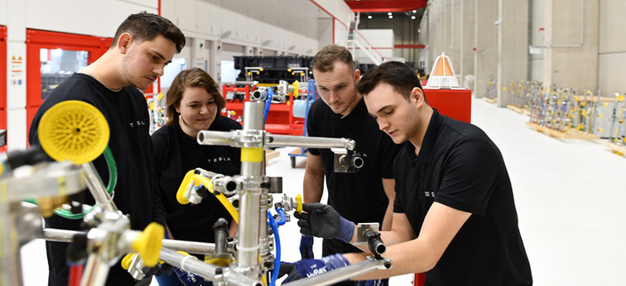 Vier Auszubildende in schwarzen T-Shirts in der Produktionsstätte Vier Auszubildende in schwarzen T-Shirts in der Produktionsstätte
