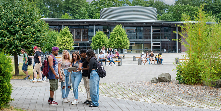 Eine Gruppe von 5 jungen Menschen vor einem Gebäude der Hochschule Schmalkalden, im Hintergrund weitere kleine Gruppen Studierender Eine Gruppe von 5 jungen Menschen vor einem Gebäude der Hochschule Schmalkalden, im Hintergrund weitere kleine Gruppen Studierender