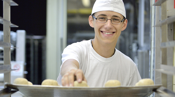 Junger Mann in Bäckerkleidung beim Bestücken des Backbleches Junger Mann in Bäckerkleidung beim Bestücken des Backbleches