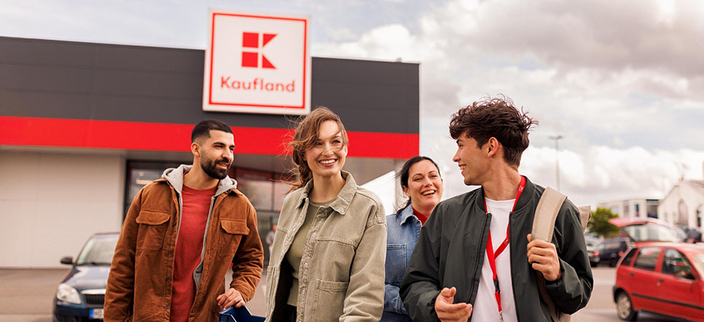 Vier junge lächelnde Personen auf dem Parkplatz vor einer Kaufland-Filiale