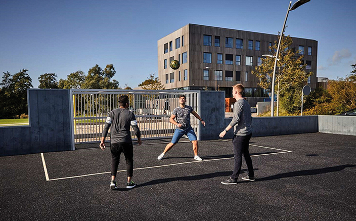 Junge ballspielende Menschen auf dem Sportplatz vor dem Universitätsgebäude Junge ballspielende Menschen auf dem Sportplatz vor dem Universitätsgebäude