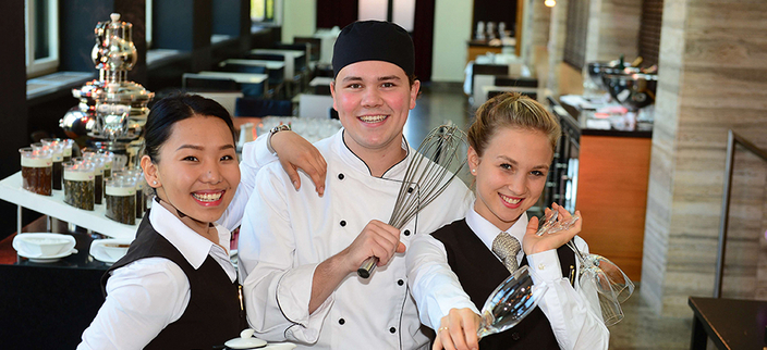 3 junge Auszubildende in Arbeitsklamotten des Gastronomiebereichs 3 junge Auszubildende in Arbeitsklamotten des Gastronomiebereichs
