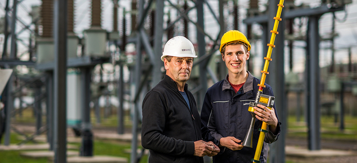Zwei Mitarbeitende mit einem Werkzeug vor einer Hochspannungsanlage