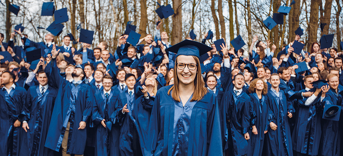 Gruppenfoto von Studierenden mit blauen Umhängen, die ihre Hüte in die Luft werfen Gruppenfoto von Studierenden mit blauen Umhängen, die ihre Hüte in die Luft werfen