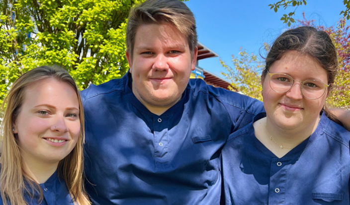 Drei Personen stehen eng nebeneinander und lächeln in die Kamera. Drei Personen stehen eng nebeneinander und lächeln in die Kamera.