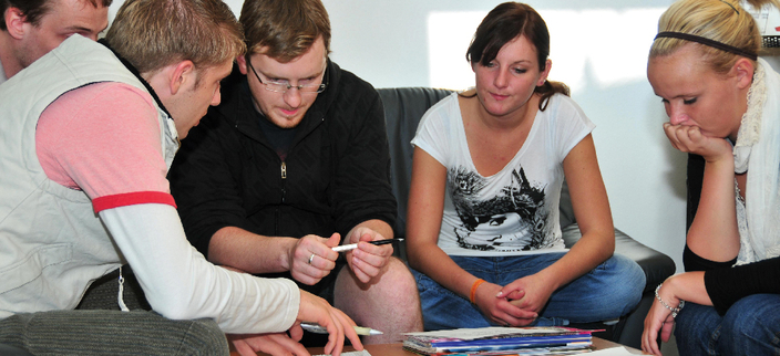 Fünf junge Personen an einem Sofatisch im Gespräch