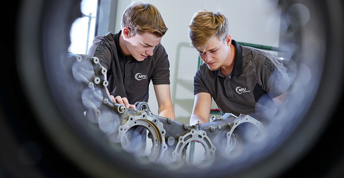 Zwei junge Menschen in Poloshirts mit Firmenlogo arbeiten an der Triebwerkstechnik Zwei junge Menschen in Poloshirts mit Firmenlogo arbeiten an der Triebwerkstechnik