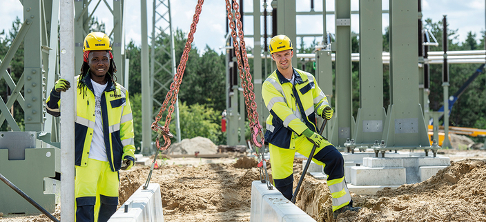 Zwei Personen in gelber Schutzkleidung mit Helm euf einer Baustelle Zwei Personen in gelber Schutzkleidung mit Helm euf einer Baustelle