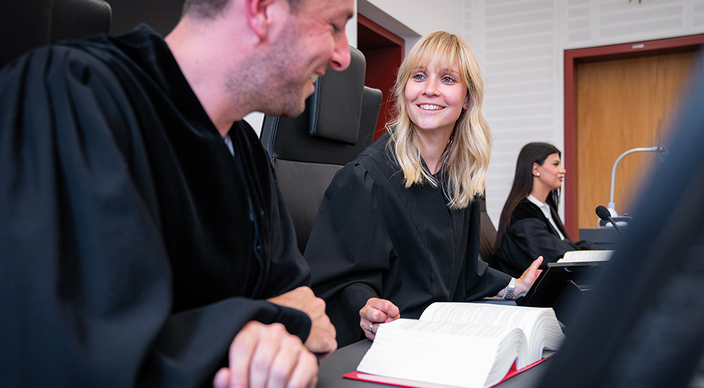 Zwei lächelnde Personen im Gericht mit einem Gesetzesbuch, im Hintergrund eine weitere Person Zwei lächelnde Personen im Gericht mit einem Gesetzesbuch, im Hintergrund eine weitere Person