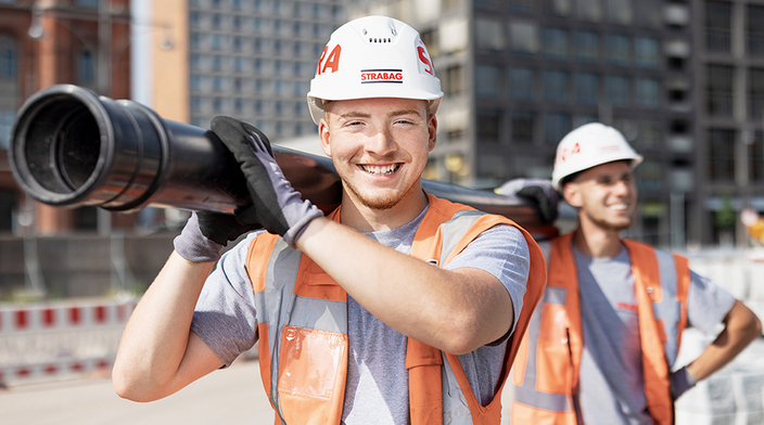 Zwei junge Männer in Arbeitskleidung tragen Rohr Zwei junge Männer in Arbeitskleidung tragen Rohr