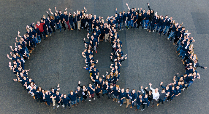 Teamfoto von oben aufgenommen, Mitarbeitende bilden die zwei ineinander verschlungenen Ringe des Logos Teamfoto von oben aufgenommen, Mitarbeitende bilden die zwei ineinander verschlungenen Ringe des Logos