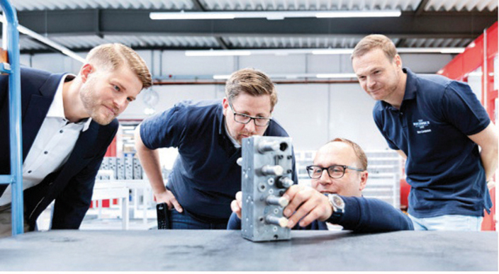 Vier Mitarbeitende begutachten ein Bauteil in der Produktionsstätte Vier Mitarbeitende begutachten ein Bauteil in der Produktionsstätte