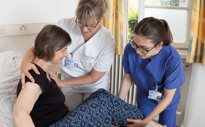 Pflegekräfte helfen einer Patientin, sich im Bett hinzusetzen Pflegekräfte helfen einer Patientin, sich im Bett hinzusetzen