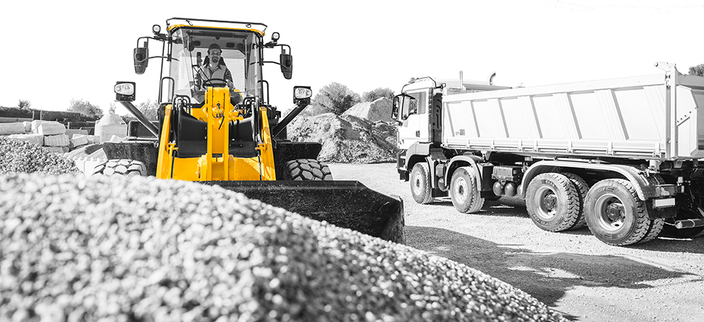 Situation auf einer Baustelle im Vordergrund des Bildes ein großer Haufen mit Kies, dahinter ein Bagger und im rechten Bildbereich ein Laster Situation auf einer Baustelle im Vordergrund des Bildes ein großer Haufen mit Kies, dahinter ein Bagger und im rechten Bildbereich ein Laster