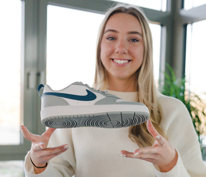 Junge Frau hält lächelnd einen Nike-Schuh in die Kamera Junge Frau hält lächelnd einen Nike-Schuh in die Kamera
