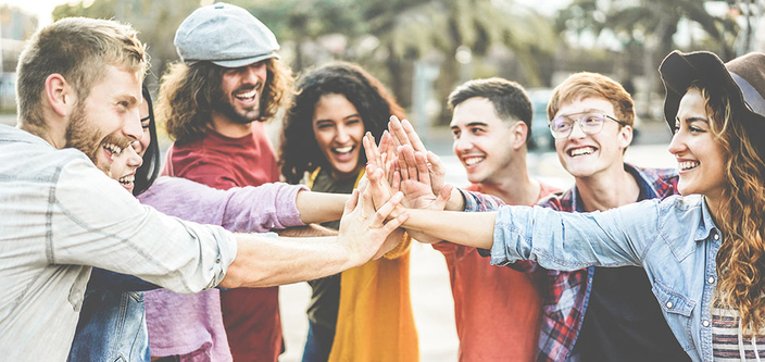 Junge Menschen bilden einen Kreis und halten in der Mitte ihre Hände zusammen um den Teamgedanken zu symbolisieren