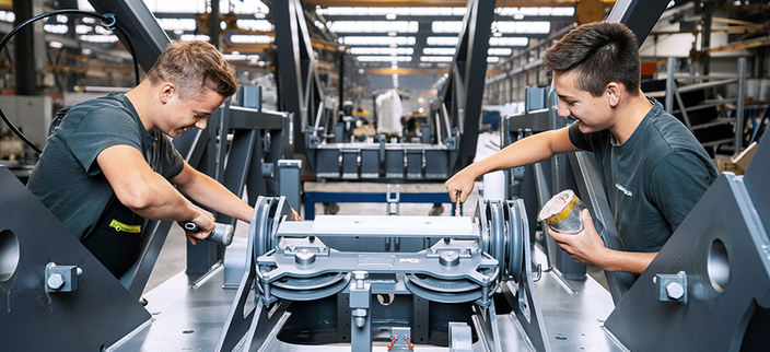Zwei junge Menschen in schwarzen T-Shirts mit Firmenlogo arbeiten an einer Maschine