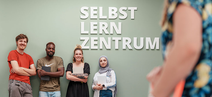 Studierende der Evangelischen Hochschule Rheinland-Westfalen-Lippe vor einer Wand mit der Aufschrift Selbstlernzentrum 