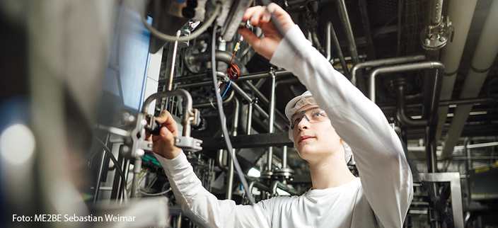 Junge Person mit Schutzbrille bedient eine Maschine in der Herstellung Junge Person mit Schutzbrille bedient eine Maschine in der Herstellung