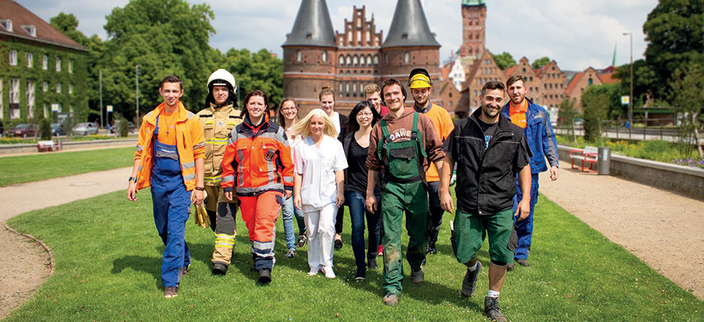 12 junge Menschen laufen von einem Gebäude auf die Kamera zu. Sie haben unterschiedliche Arbeitskleidung an, Wie Bauhelme, Feuerwehrausrüstung etc. 12 junge Menschen laufen von einem Gebäude auf die Kamera zu. Sie haben unterschiedliche Arbeitskleidung an, Wie Bauhelme, Feuerwehrausrüstung etc.