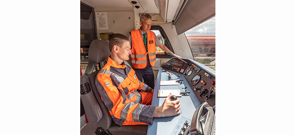 Ein junger Mann im Cockpit einer Erfurter Bahn am Steuerhebel, neben ihm steht ein Mann in Sicherheitsweste und erklärt ihm die Anzeigen.