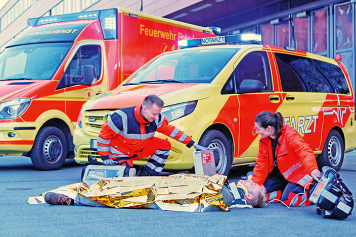 Personen versorgen Verwundeten vor einem Rettungswagen. Personen versorgen Verwundeten vor einem Rettungswagen.