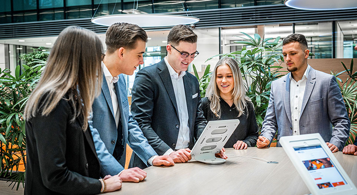 Bankfachleute stehen gemeinsam an einem Tisch und schauen auf ein Tablet