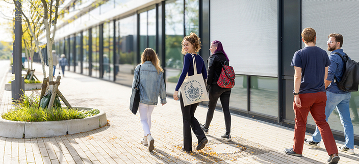 Studentengruppe von 5 Personen läuft durch eine Gasse mit kleinen Bäumen. Die Sonne scheint angenehm von vorne Studentengruppe von 5 Personen läuft durch eine Gasse mit kleinen Bäumen. Die Sonne scheint angenehm von vorne