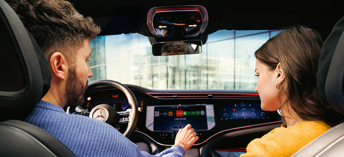 Zwei Personen im Auto von der Rückbank aus aufgenommen, eine davon stellt am Bordcomputer etwas ein Zwei Personen im Auto von der Rückbank aus aufgenommen, eine davon stellt am Bordcomputer etwas ein