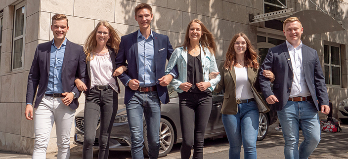 Sechs junge lächelnde Personen Arm in Arm vor dem Firmengebäude Sechs junge lächelnde Personen Arm in Arm vor dem Firmengebäude