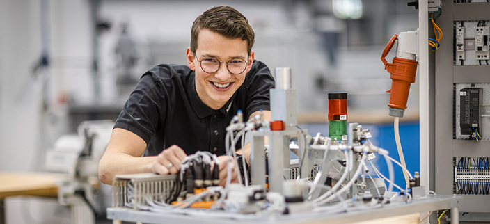Person lächelt in die Kamera im Vordergrund elektrisches Gerät. 