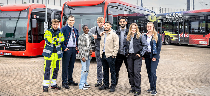 Acht Auszubildende aus verschiedenen Bereichen, im Hintergrund drei Busse der BSAG