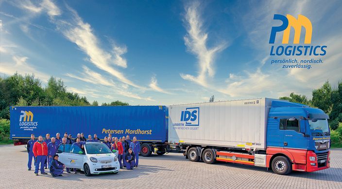 Gruppenfoto der Mitarbeitenden auf einem Parkplatz mit PKW und LKW im Hintergrund Gruppenfoto der Mitarbeitenden auf einem Parkplatz mit PKW und LKW im Hintergrund