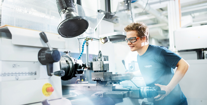 Junge Person mit Schutzbrille bei der Arbeit an einer Masschine Junge Person mit Schutzbrille bei der Arbeit an einer Masschine