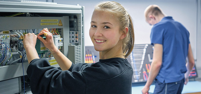 Eine Person arbeitet lächelnd an einem Schaltschrank mit vielen Kabeln. 