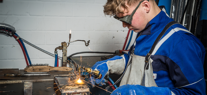 Junger Mensch in Arbeitskleidung mit Schutzbrille beim Schweißen Junger Mensch in Arbeitskleidung mit Schutzbrille beim Schweißen