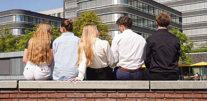 Jugendliche sitzen auf einer Mauer vor Firmengebäude Jugendliche sitzen auf einer Mauer vor Firmengebäude