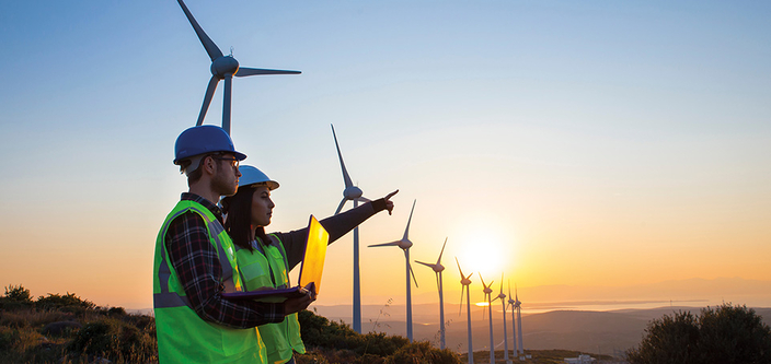 Zwei Personen und Windkrafträder im Sonnenuntergang