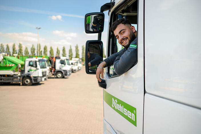 Junger Mensch im Nehlsen-LKW dreht sich um und lächelt in die Kamera, im Hintergrund weitere LKWs