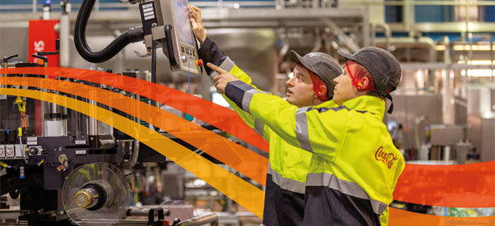 2 Mitarbeitende mit Bauhelmen in einer Produktionsstätte bedienen einen Bildschirm einer Maschine 2 Mitarbeitende mit Bauhelmen in einer Produktionsstätte bedienen einen Bildschirm einer Maschine