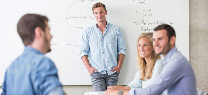 Personengruppe vor einem Whiteboard, darauf zu sehen unterschiedliche Formeln. Personengruppe vor einem Whiteboard, darauf zu sehen unterschiedliche Formeln.