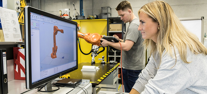 Eine Person sieht auf einen Monitor, eine andere arbeitet an einem mechanischem Arm. Eine Person sieht auf einen Monitor, eine andere arbeitet an einem mechanischem Arm.